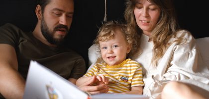 A happy family reading together, featuring parents and their smiling child enjoying a book indoors.