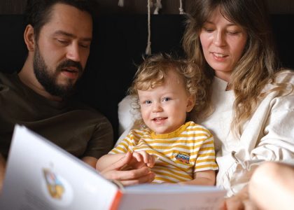 A happy family reading together, featuring parents and their smiling child enjoying a book indoors.